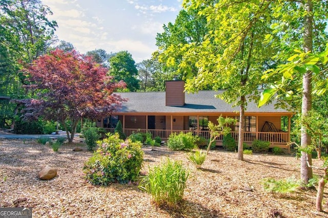 rear view of house featuring covered porch, a shingled roof, and a chimney