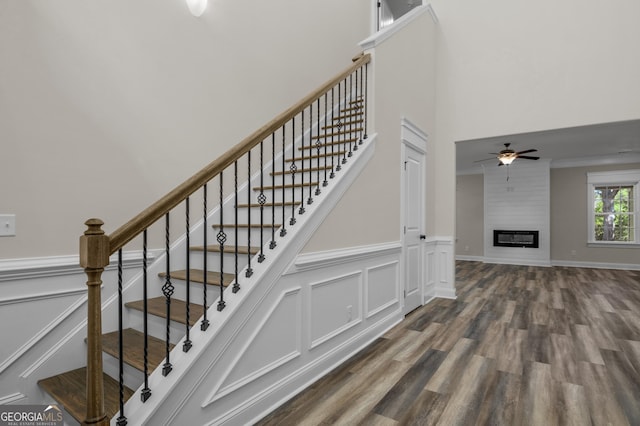 243 Barrington Oaks Dr, Brunswick, GA 31523 - staircase featuring wood finished floors, wainscoting, ceiling fan, a towering ceiling, and a fireplace