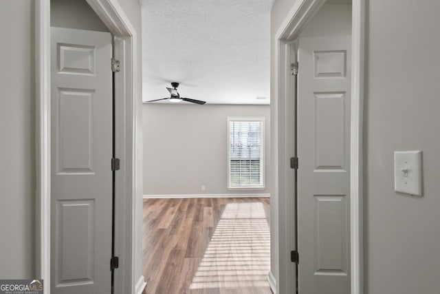hallway featuring a textured ceiling, baseboards, and wood finished floors
