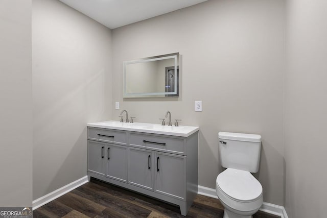 bathroom featuring baseboards, double vanity, toilet, wood finished floors, and a sink