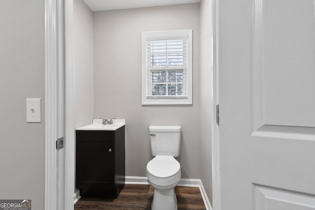 half bath featuring baseboards, wood finished floors, toilet, and vanity