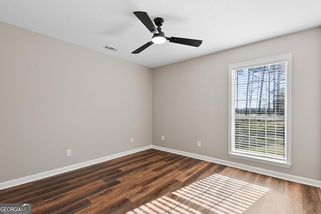 empty room with dark wood-style floors, visible vents, baseboards, and a ceiling fan