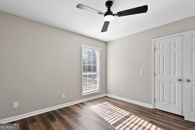 unfurnished bedroom featuring a closet, a ceiling fan, a textured ceiling, baseboards, and dark wood-type flooring