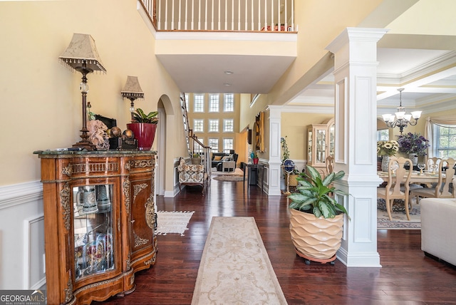 entrance foyer featuring a high ceiling, ornate columns, dark wood-style floors, arched walkways, and a notable chandelier