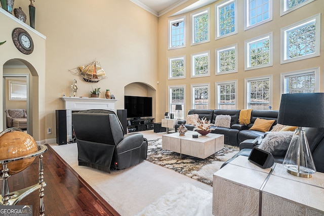 living room with a fireplace with flush hearth, arched walkways, a towering ceiling, baseboards, and ornamental molding