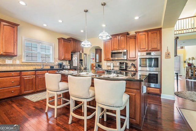 kitchen with dark wood-style floors, appliances with stainless steel finishes, a sink, and a breakfast bar