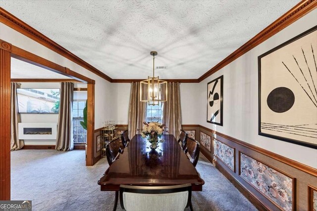 carpeted dining area with a textured ceiling, a wainscoted wall, ornamental molding, and an inviting chandelier