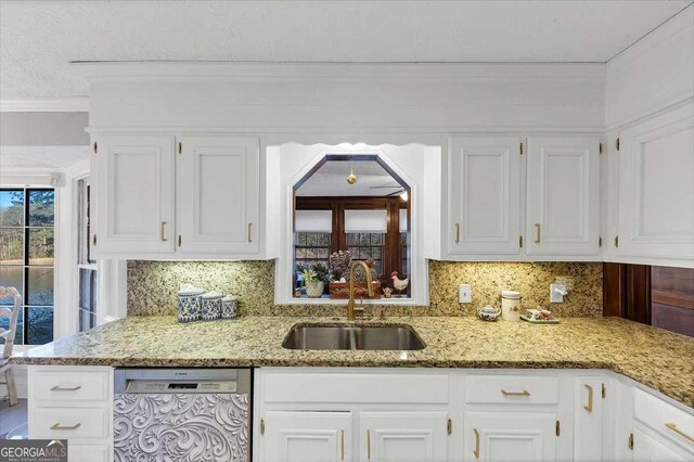 kitchen featuring dishwasher, light stone countertops, white cabinetry, a sink, and backsplash