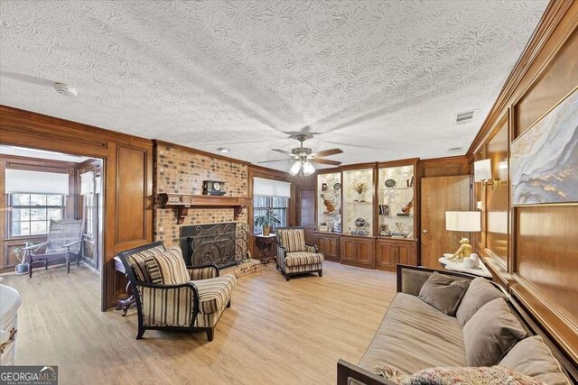 living room with light wood finished floors, ceiling fan, a fireplace, and visible vents