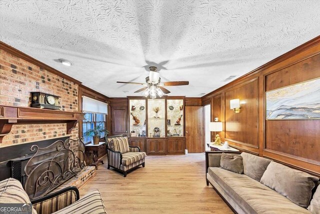 living area with crown molding, light wood-style floors, wooden walls, a ceiling fan, and a fireplace