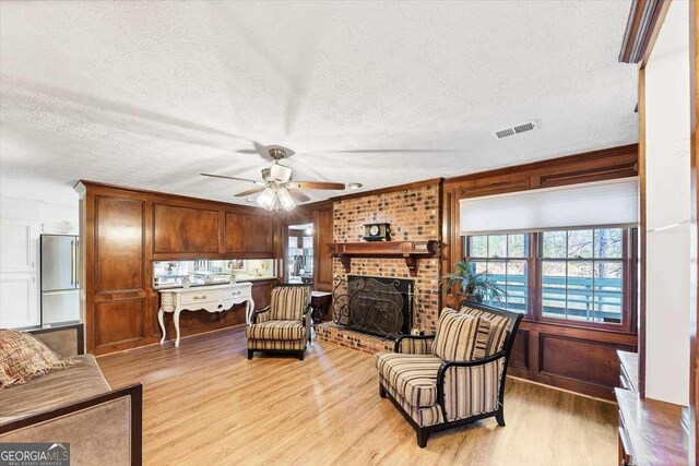 living area with visible vents, a healthy amount of sunlight, light wood-style floors, and a brick fireplace