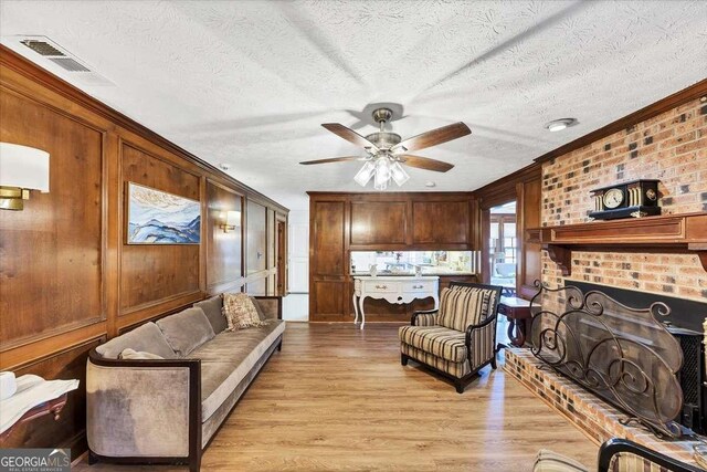 living area with light wood-type flooring, a textured ceiling, ceiling fan, visible vents, and a fireplace