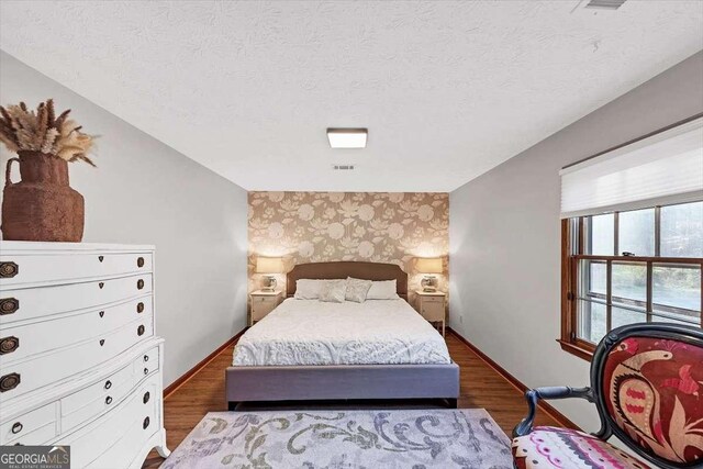 bedroom with baseboards, wallpapered walls, wood finished floors, and a textured ceiling