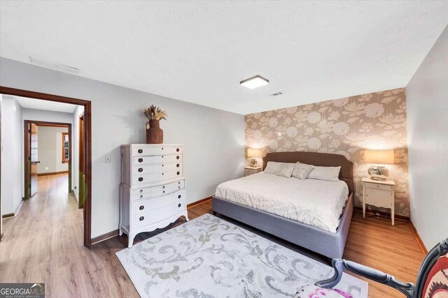 bedroom with baseboards, wallpapered walls, light wood-type flooring, and an accent wall
