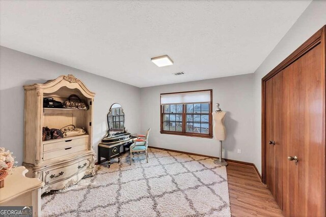 living area with light wood finished floors, baseboards, visible vents, and a textured ceiling