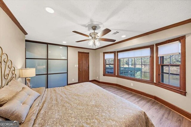 bedroom with a textured ceiling, visible vents, baseboards, ornamental molding, and wood finished floors