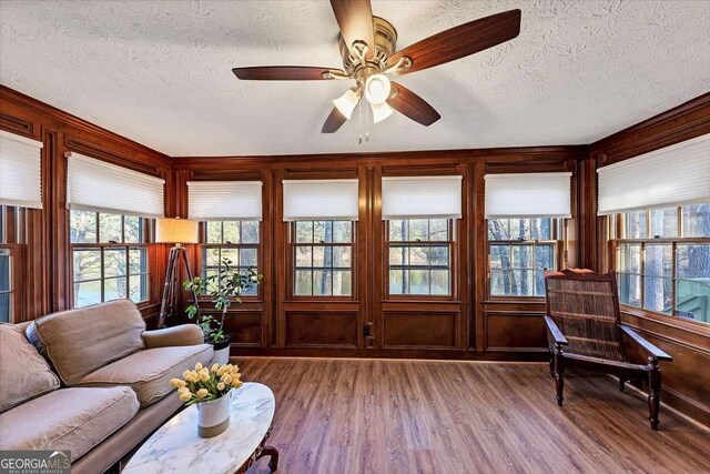 living room with a textured ceiling, wood walls, ceiling fan, and wood finished floors