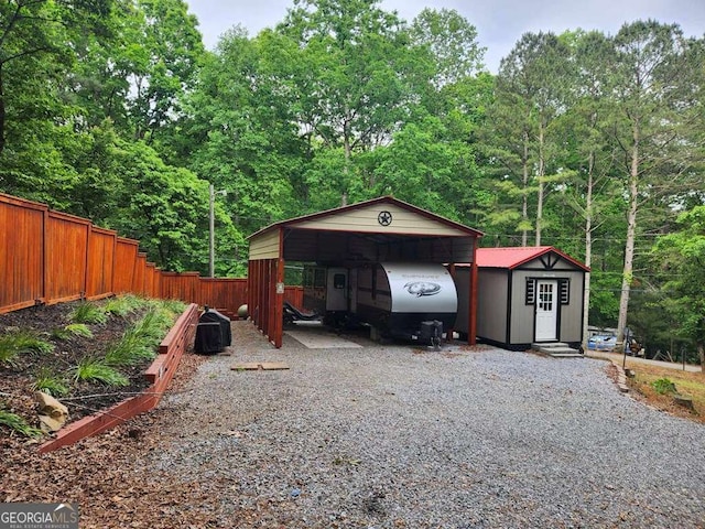 garage featuring gravel driveway, a carport, and fence