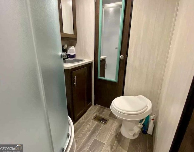 bathroom featuring visible vents, a shower stall, toilet, vanity, and wood tiled floor