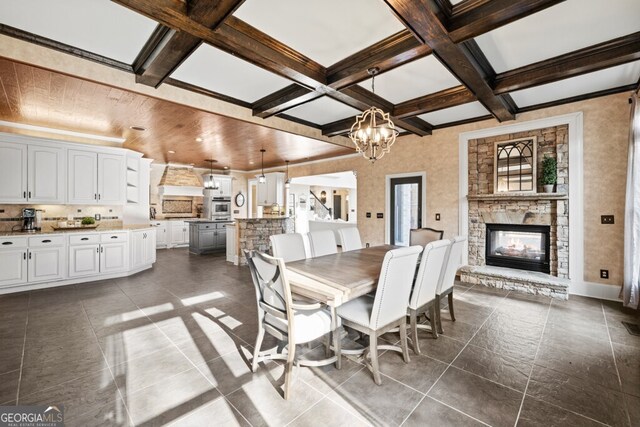 3491 Falls Branch Ct, Buford, GA 30519 - dining room featuring coffered ceiling, beamed ceiling, a stone fireplace, a chandelier, and dark tile patterned floors
