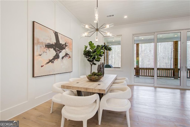 dining space with visible vents, light wood-type flooring, baseboards, an inviting chandelier, and ornamental molding