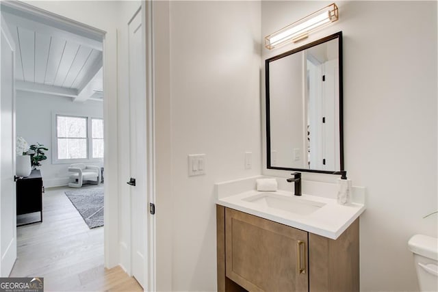 half bathroom featuring vanity, toilet, beam ceiling, and wood finished floors