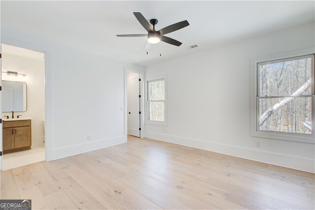 unfurnished bedroom featuring visible vents, baseboards, a sink, light wood-style flooring, and ensuite bath