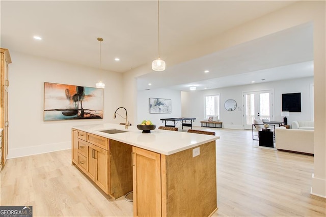 kitchen featuring hanging light fixtures, a sink, light wood-style flooring, recessed lighting, and a center island with sink