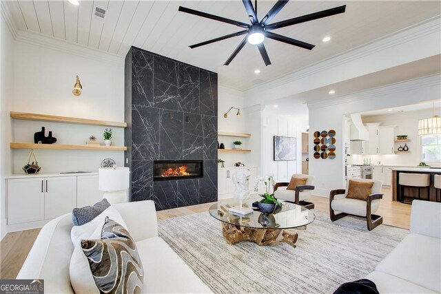 living area with recessed lighting, crown molding, light wood-type flooring, and a premium fireplace