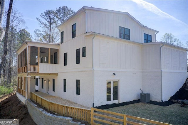 view of property exterior featuring central AC, brick siding, board and batten siding, a sunroom, and french doors