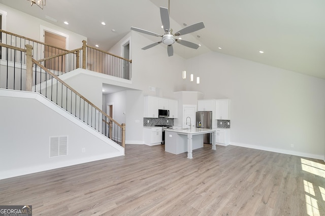 unfurnished living room with visible vents, a ceiling fan, stairway, light wood finished floors, and high vaulted ceiling