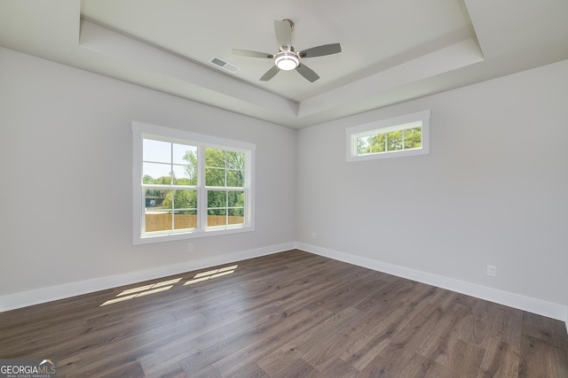 spare room with dark wood-style flooring, visible vents, baseboards, and a raised ceiling