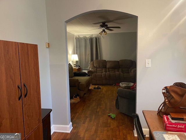 living room featuring baseboards, arched walkways, ceiling fan, and dark wood-style flooring