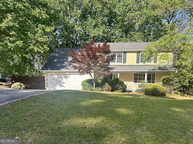 traditional-style home featuring covered porch, a garage, fence, and a front yard