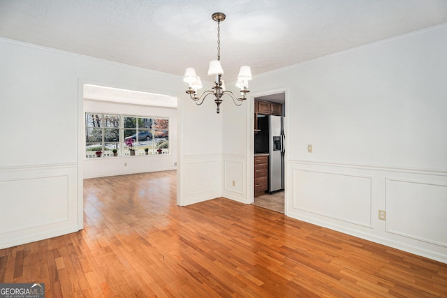 unfurnished dining area with crown molding, light wood finished floors, wainscoting, and a chandelier