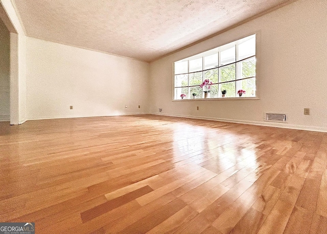 spare room featuring light wood-type flooring, a textured ceiling, baseboards, and visible vents