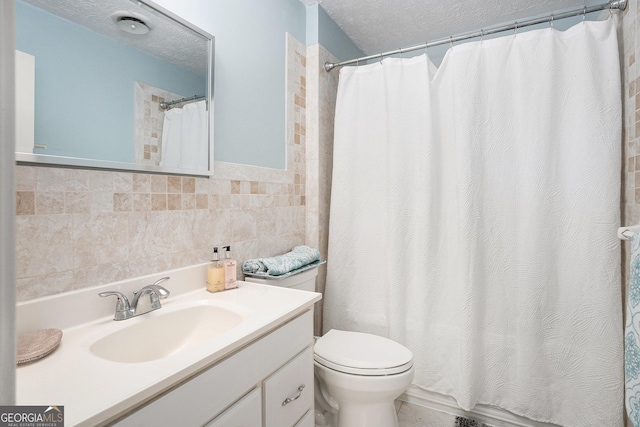 bathroom with a textured ceiling, tile walls, curtained shower, vanity, and toilet