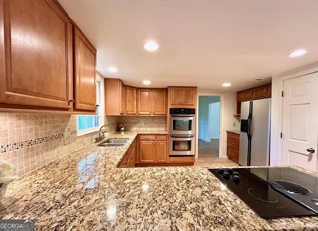 kitchen featuring light stone counters, a sink, brown cabinetry, stainless steel appliances, and backsplash