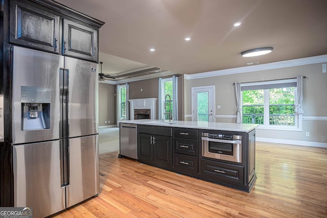 kitchen featuring a sink, light countertops, crown molding, stainless steel appliances, and light wood-style flooring