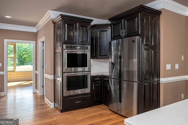 kitchen with crown molding, light wood-type flooring, appliances with stainless steel finishes, light stone counters, and baseboards