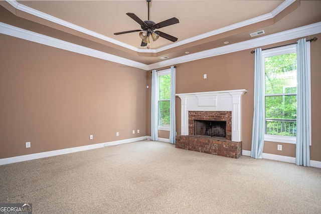 unfurnished living room featuring baseboards, ornamental molding, a raised ceiling, a brick fireplace, and ceiling fan