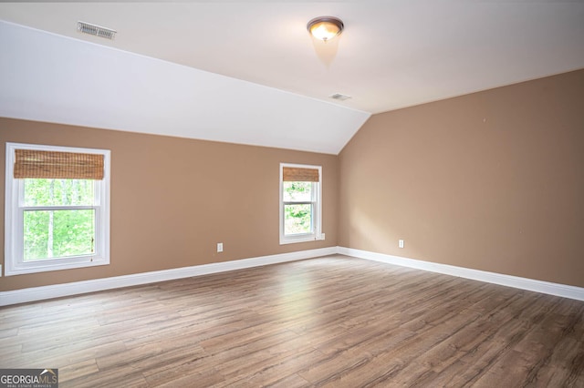 spare room featuring wood finished floors, visible vents, baseboards, and lofted ceiling