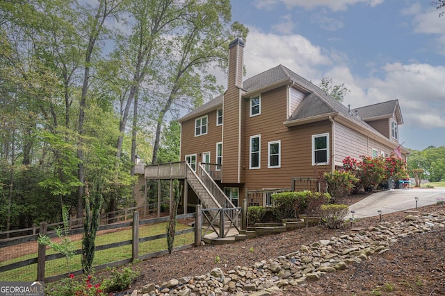 rear view of house featuring stairway, roof with shingles, fence, a chimney, and a deck