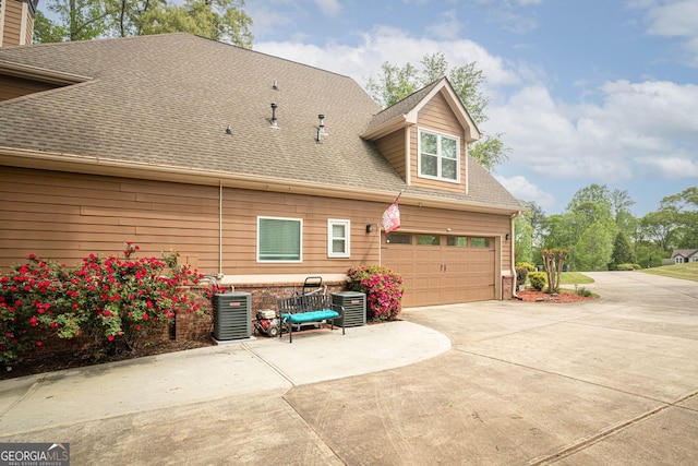 back of property featuring a garage, roof with shingles, brick siding, driveway, and central AC unit