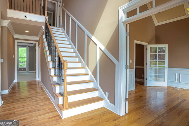 stairs with a decorative wall, wainscoting, crown molding, and wood finished floors