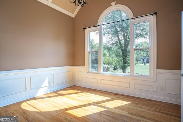 interior space with an inviting chandelier, vaulted ceiling, a wainscoted wall, a decorative wall, and light wood finished floors