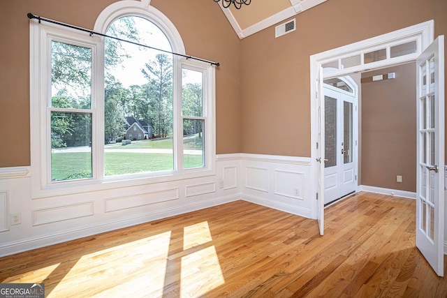 empty room with visible vents, a wainscoted wall, lofted ceiling, french doors, and light wood finished floors