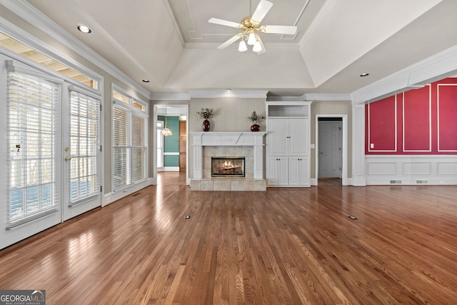 unfurnished living room with a tile fireplace, ornamental molding, wood finished floors, a ceiling fan, and a raised ceiling