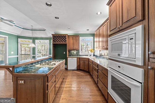 kitchen with decorative backsplash, white appliances, brown cabinets, dark countertops, and light wood-type flooring