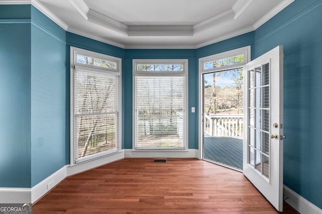 unfurnished dining area with crown molding, wood finished floors, a raised ceiling, and a healthy amount of sunlight